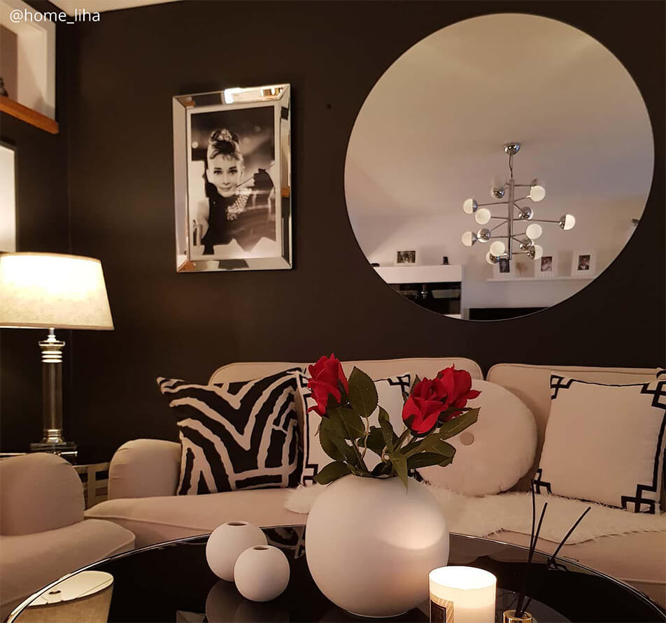Stue med mørk veggfarge, hvit sofa og stort, rundt speil